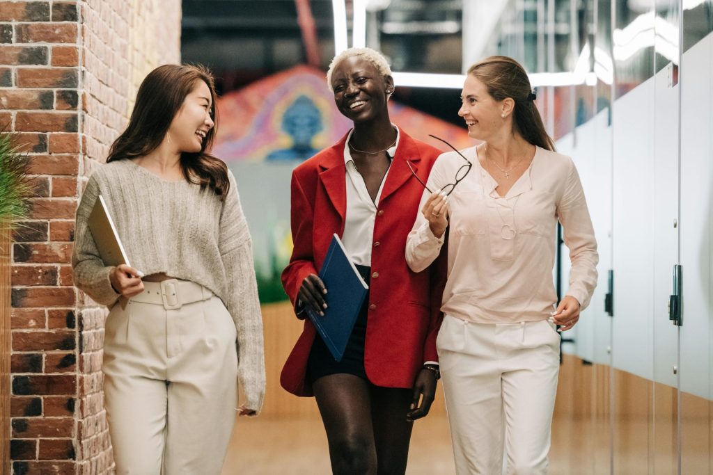 Group of young glad businesswomen in trendy elegant outfits smiling and discussing business strategy in contemporary workspace