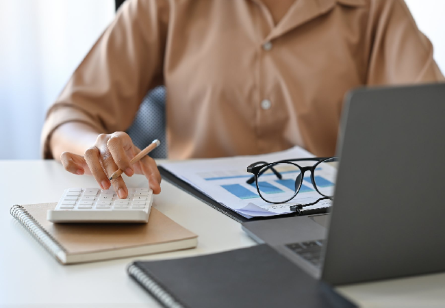 Professional working in the office while using the calculator and a laptop